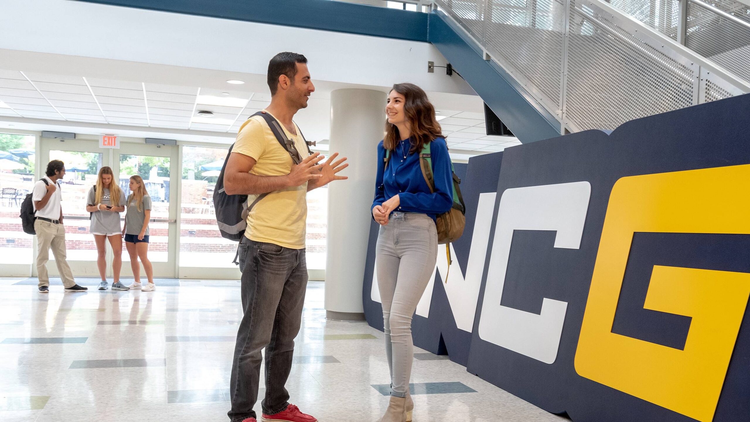 Students talking in front of the UNCG sign inside Moran Commons.