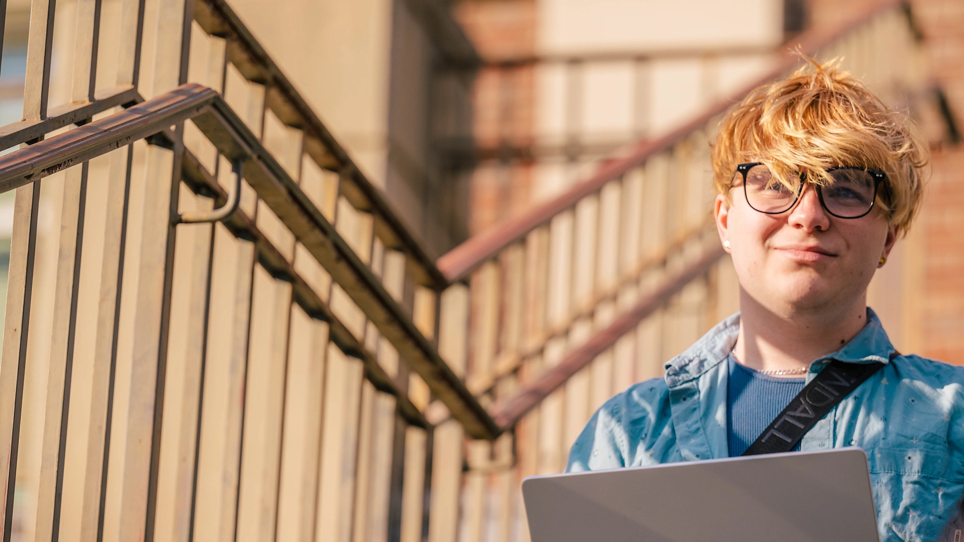 A UNCG student sitting on a flight of stairs while using a laptop.